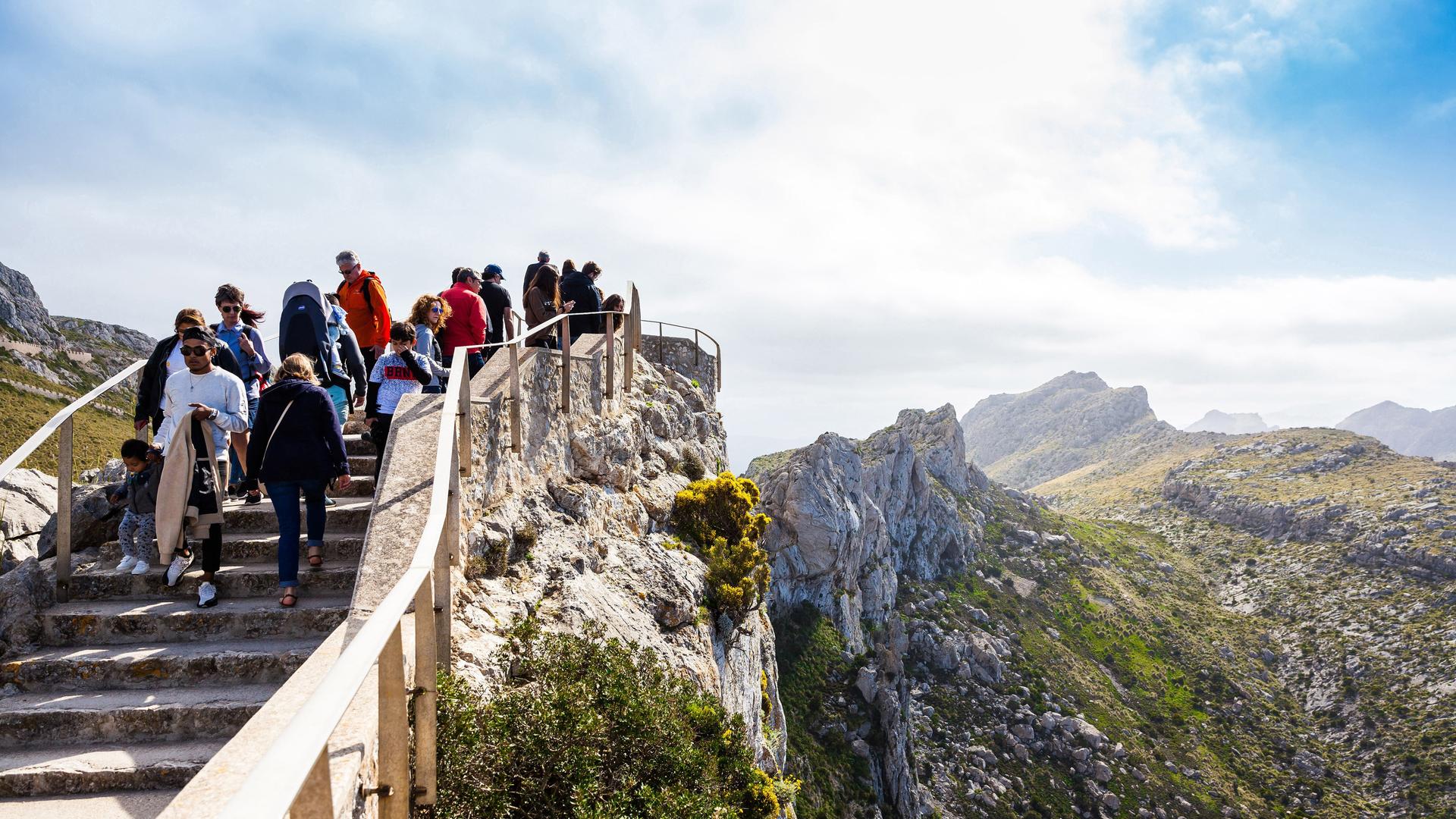 Wanderer gehen eine Treppe in den Bergen hinunter, der Himmel ist strahlend blau, es ist Sommer. 