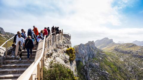 Wanderer gehen eine Treppe in den Bergen hinunter, der Himmel ist strahlend blau, es ist Sommer. 