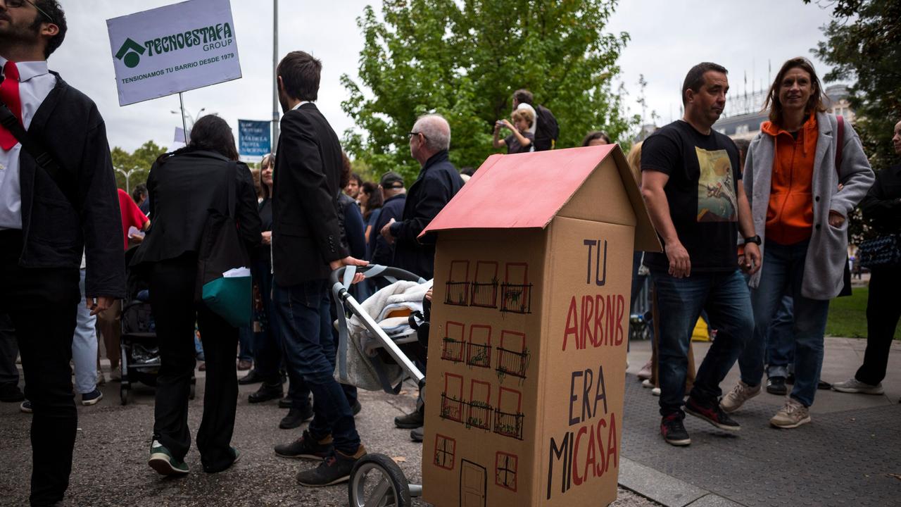 Menschen demonstieren in Madrid für bezahlbaren Wohnraum und gegen Vermietungen von Ferienwohnungen durch Airbnb. Ein Teilnehmer hat ein Papphaus auf einen Kinderwagen montiert auf dem "Tu Airbn era mi casa" steht (Dein Airbnb war mein Zuhause).