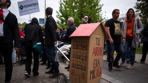 Menschen demonstieren in Madrid für bezahlbaren Wohnraum und gegen Vermietungen von Ferienwohnungen durch Airbnb. Ein Teilnehmer hat ein Papphaus auf einen Kinderwagen montiert auf dem "Tu Airbn era mi casa" steht (Dein Airbnb war mein Zuhause).