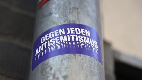 Ein Sticker mit der Aufschrift "Gegen jeden Antisemitismus" hängt an einem Laternenmast.