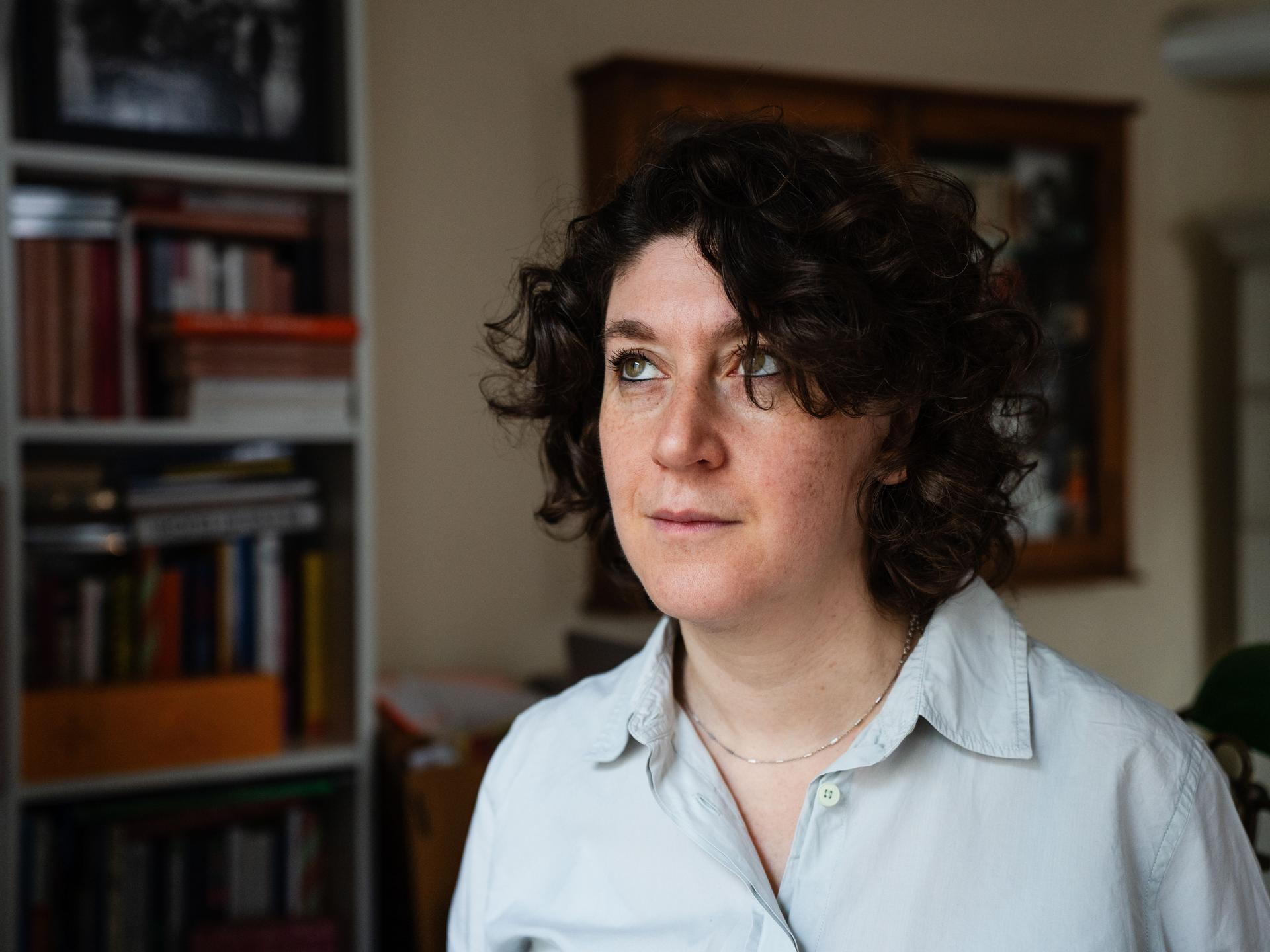 Eine Frau mit dunklen lockigen Haaren trägt ein weißes Hemd. Sie steht in einem Raum und blickt nach oben. Es ist die Autorin Lena Gorelik.