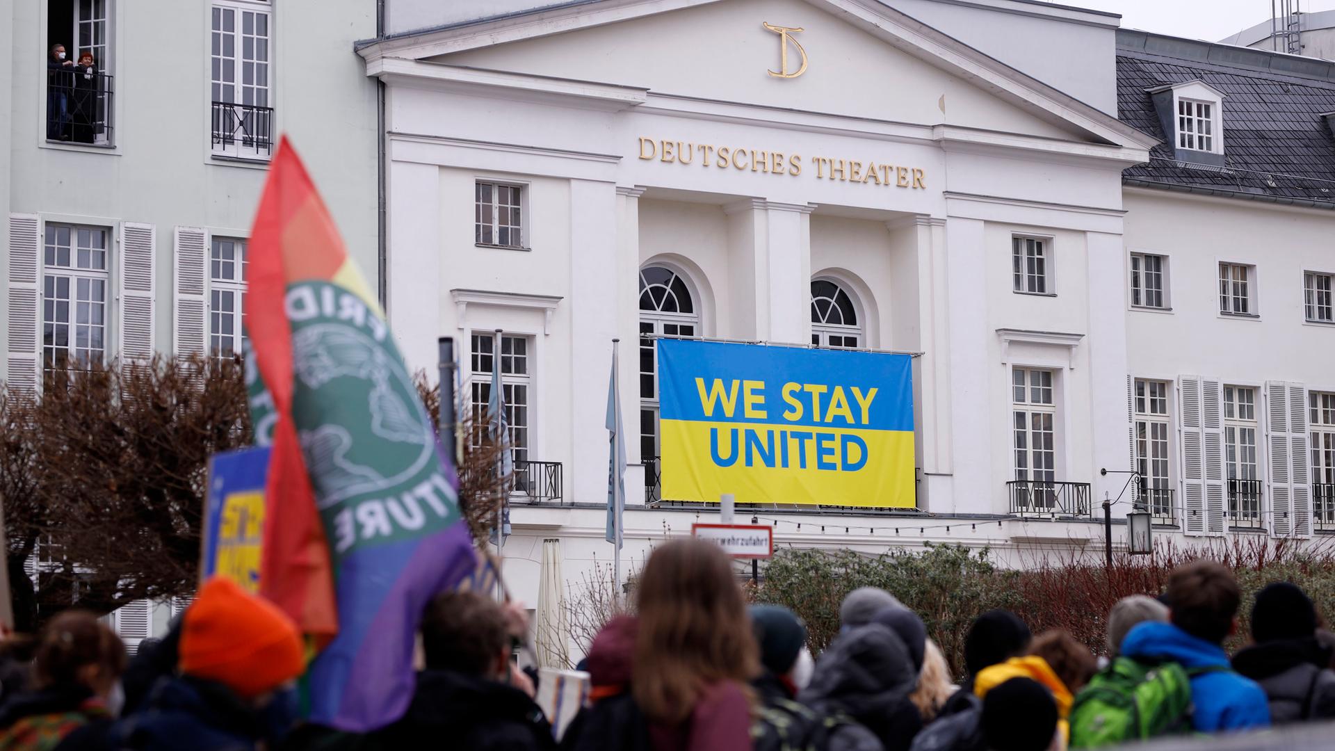 Demonstration gegen den Krieg Russlands in der Ukraine vor dem Deutschen Theater, an dem ein Banner in ukrainischen Farben mit dem Schriftzug "Stay United" hängt.