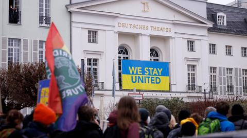 Demonstration gegen den Krieg Russlands in der Ukraine vor dem Deutschen Theater, an dem ein Banner in ukrainischen Farben mit dem Schriftzug "Stay United" hängt.