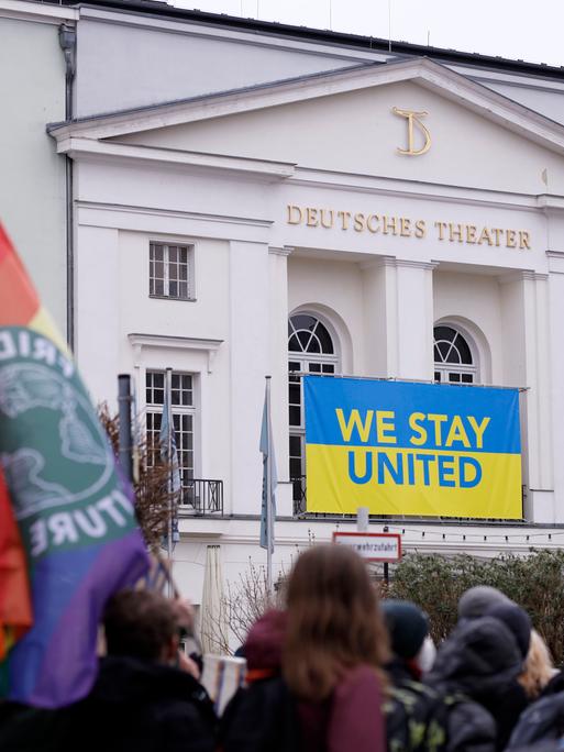 Demonstration gegen den Krieg Russlands in der Ukraine vor dem Deutschen Theater, an dem ein Banner in ukrainischen Farben mit dem Schriftzug "Stay United" hängt.