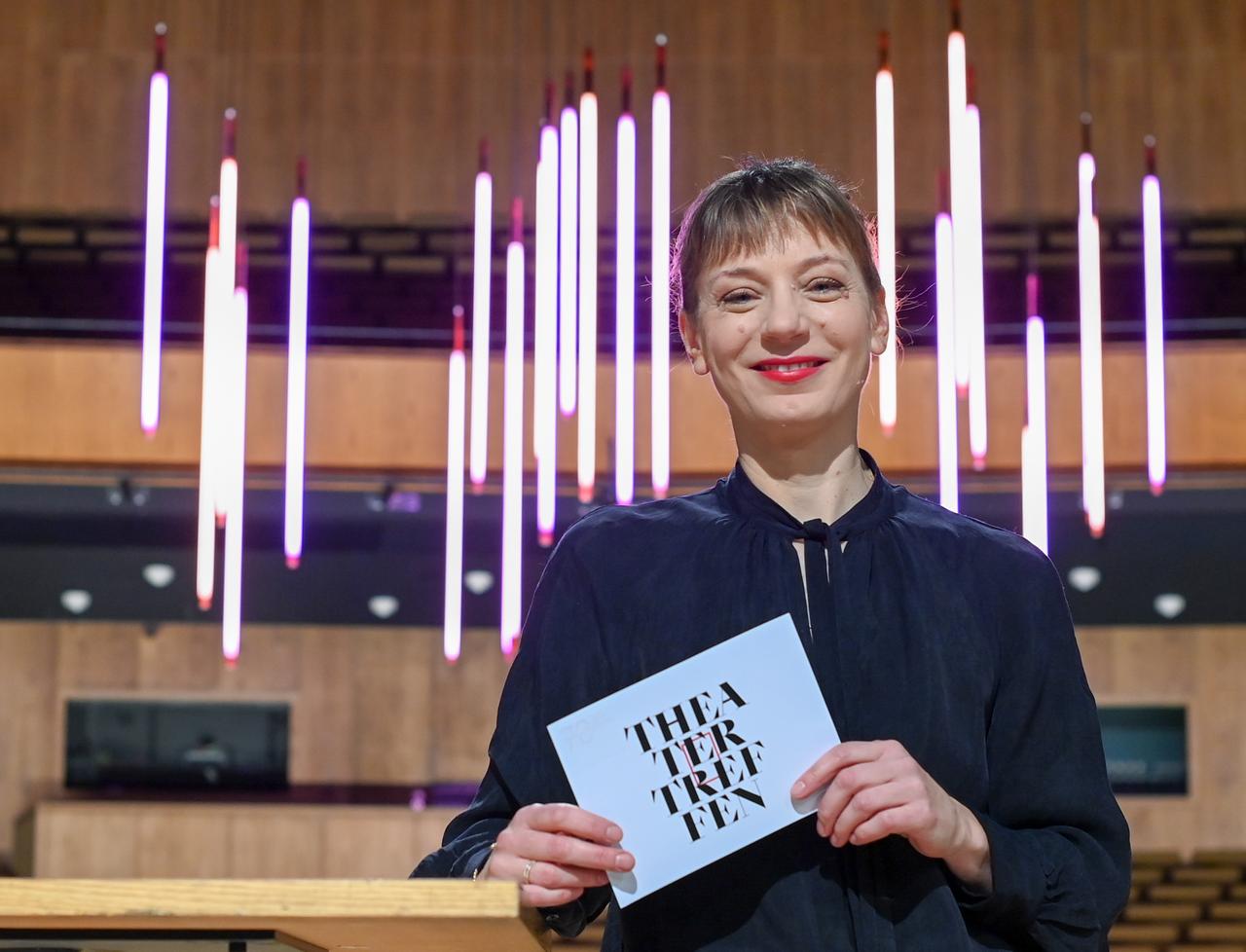 Yvonne Büdenhölzer, Leiterin des Theatertreffens der Berliner Festspiele, hält eine Karte mit der Aufschrift "Theatertreffen" in der Hand.