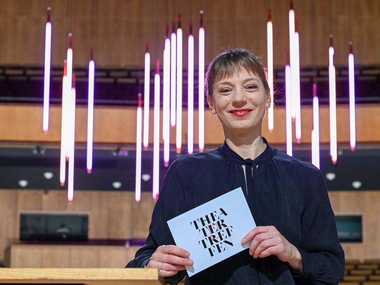 Yvonne Büdenhölzer, Leiterin des Theatertreffens der Berliner Festspiele, hält eine Karte mit der Aufschrift "Theatertreffen" in der Hand.