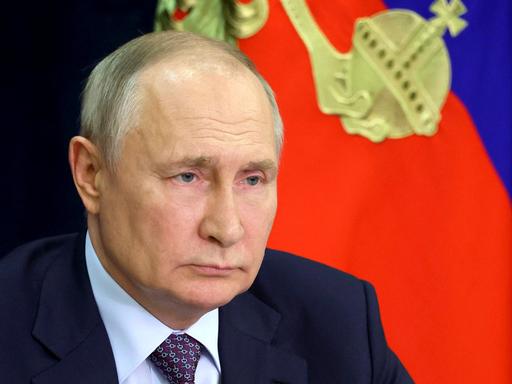 Russlands Präsident Putin sitzt vor einer blau-roten Fahne