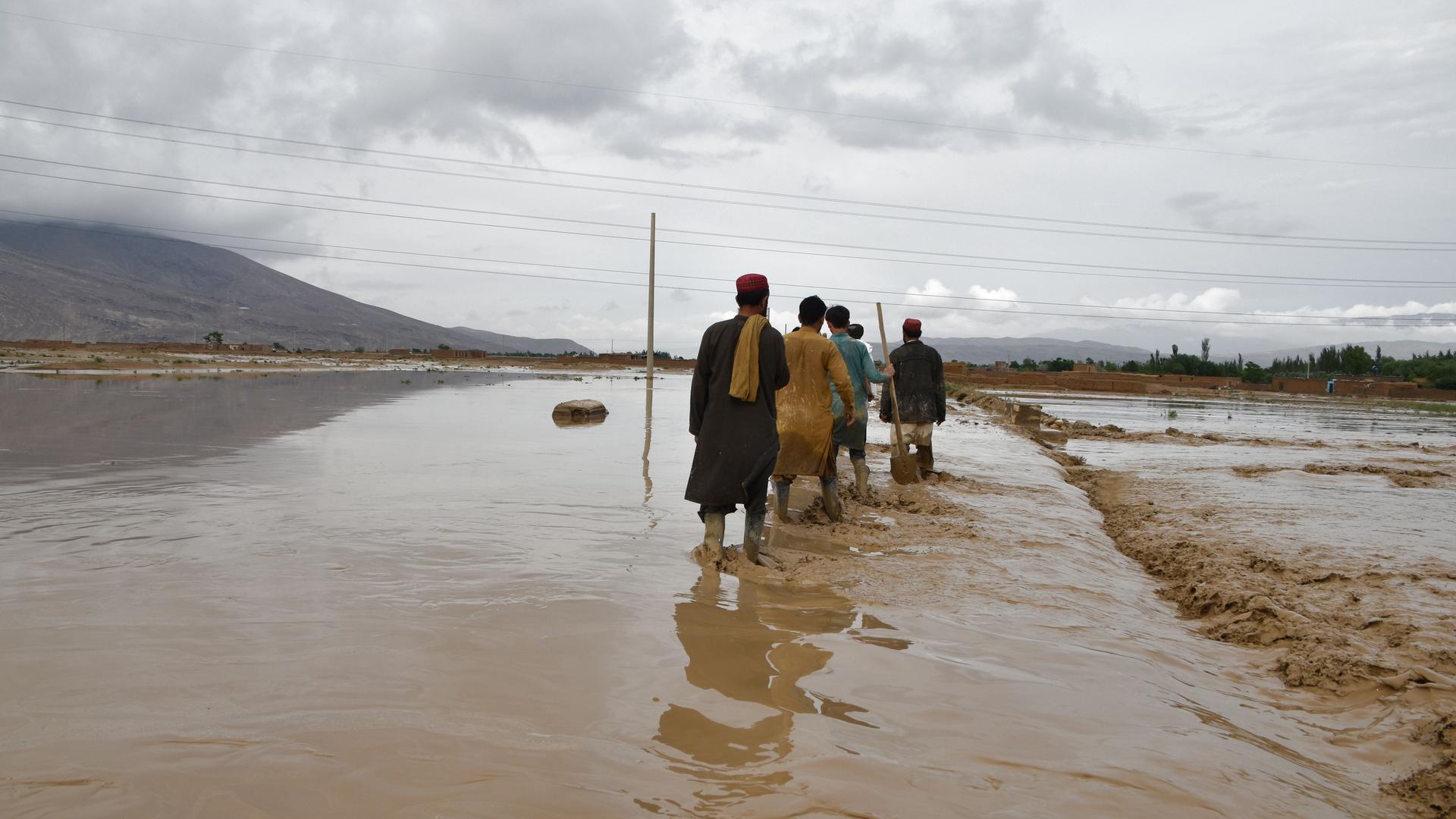 Afghanistan, Baglan: Menschen arbeiten nach heftigem Regen. Auf dem Untergrund fließt Wasser.