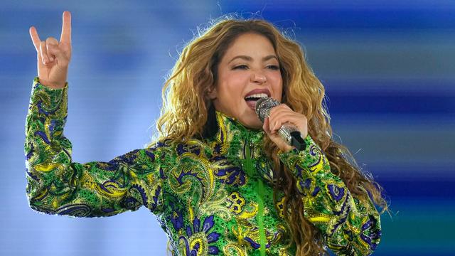 Shakira singt mit einem Mikro vor dem Mund. Die rechte Hand hält sie nach oben.