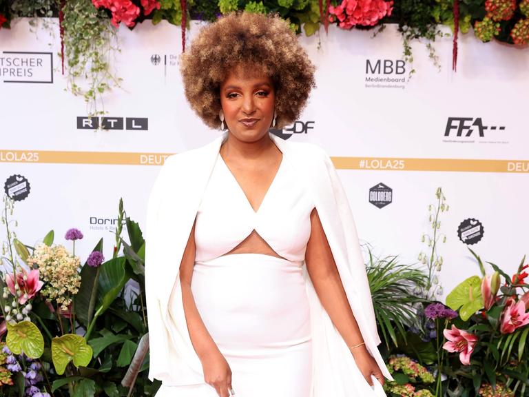 Benita Sarah Bailey bei der 75. Verleihung Deutscher Filmpreis. Sie trägt ein weißes Kleid und schaut in die Kamera.