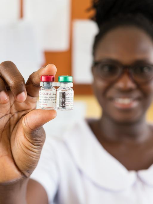 Eine Mitarbeiterin der Poliklinik in Capecoast hält zwei Döschen mit dem Impfstoff Mosquirix in die Kamera