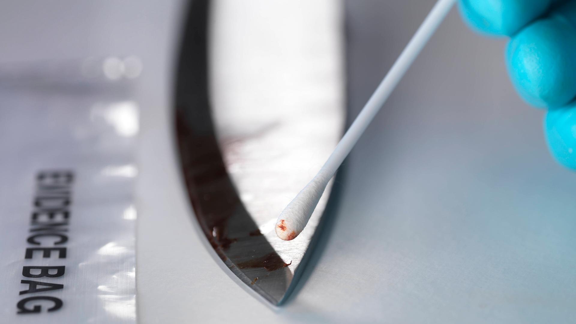 Ein Ermittler nimmt mit einen Wattestäbchen eine DNA-Probe von einem blutigen Messer.