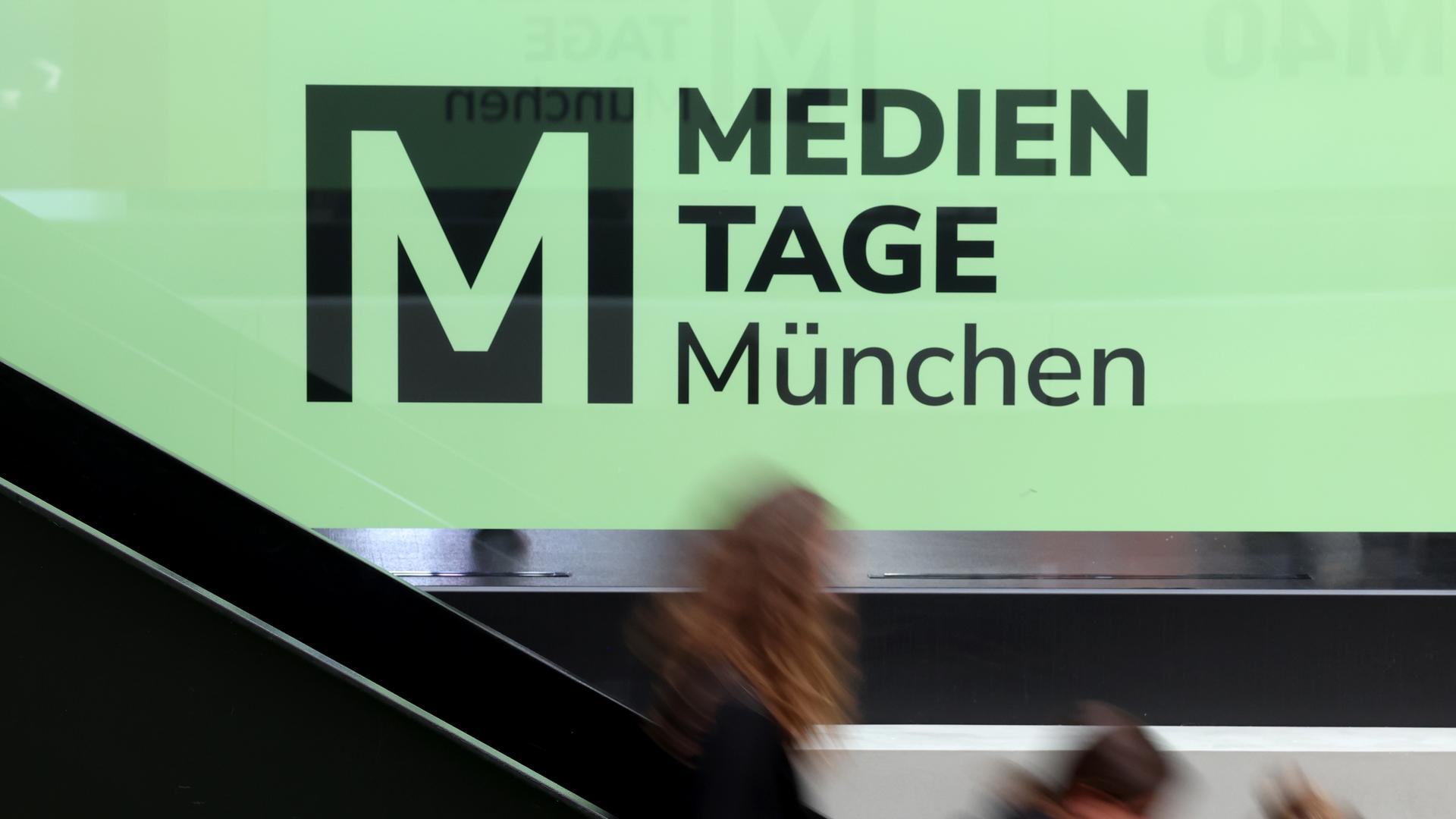 Besucher der 40. Medientage München gehen im House of Communication vor dem Schriftzug «MEDIEN TAGE München» auf einer Treppe.