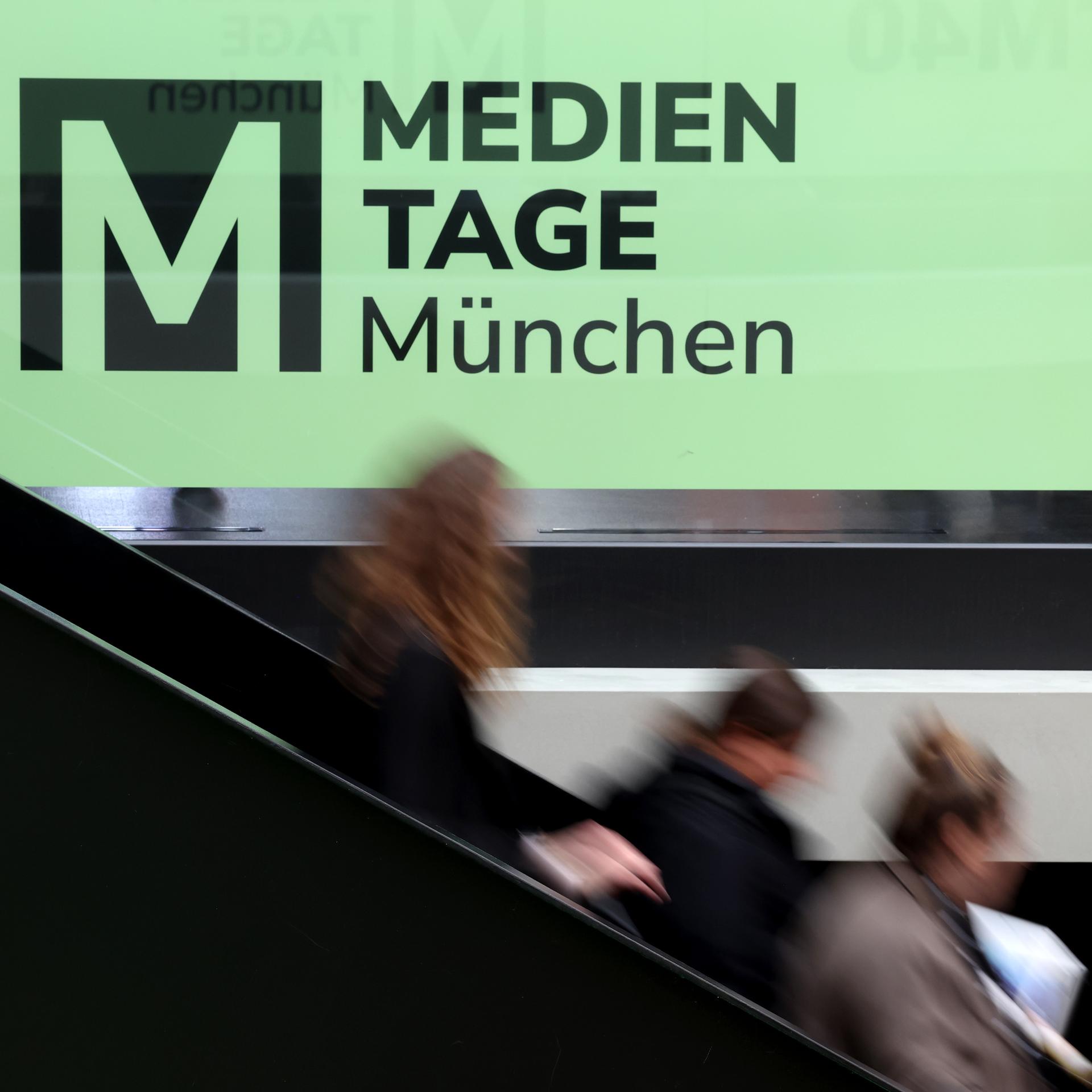 Besucher der 40. Medientage München gehen im House of Communication vor dem Schriftzug «MEDIEN TAGE München» auf einer Treppe.