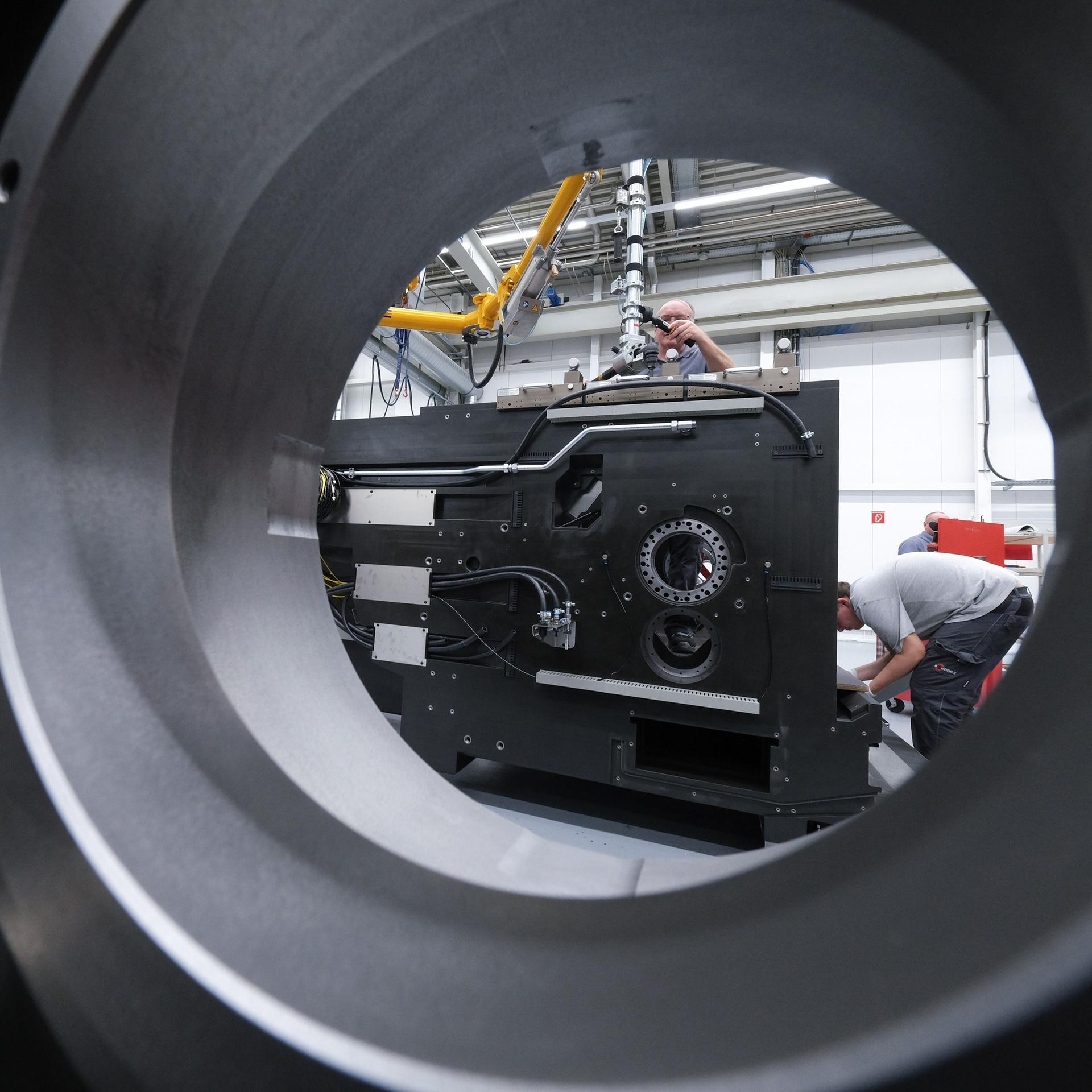 In einer Montagehalle eines Maschinenbauers werden Maschinen montiert. Ein Mann beugt sich, um eine Arbeit durchzuführen.