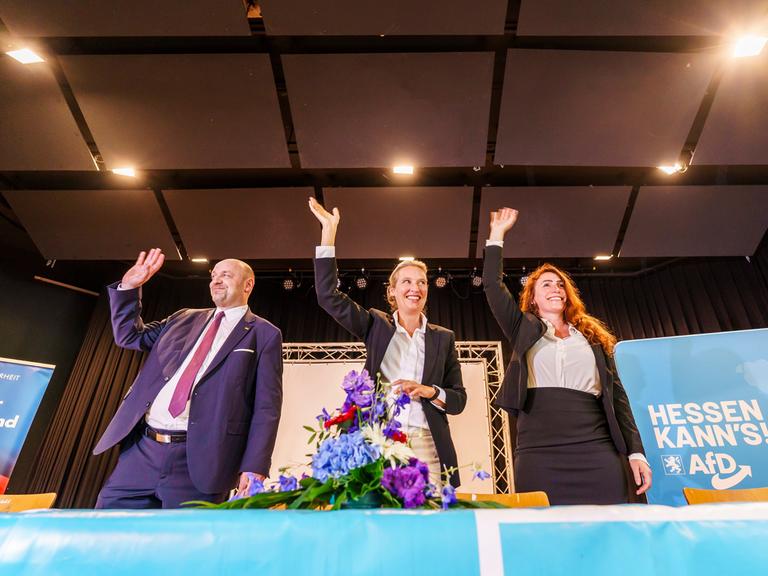 Robert Lambrou (l-r, AfD), AfD-Landesvorsitzender/Spitzenkandidat zur Landtagswahl, Alice Weidel (AfD), Bundesparteivorsitzende, und Mariana Harder-Kühnel (AfD), eine von drei stellvertretenden Bundessprechern ihrer Partei, stehen winkend und lachend auf dem Podium zusammen. 
