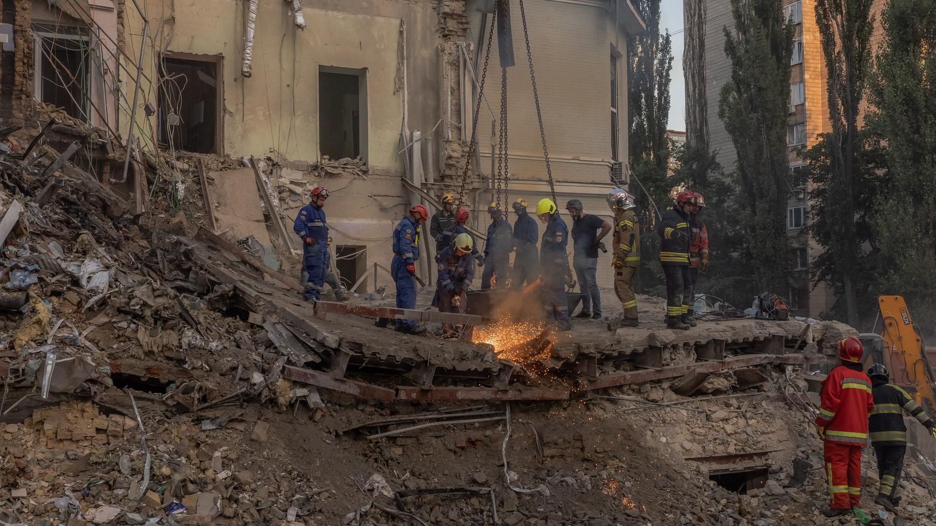 Menschen mit Schutzanzügen und Helmen stehen auf den Trümmern des Krankenhauses und schweißen.