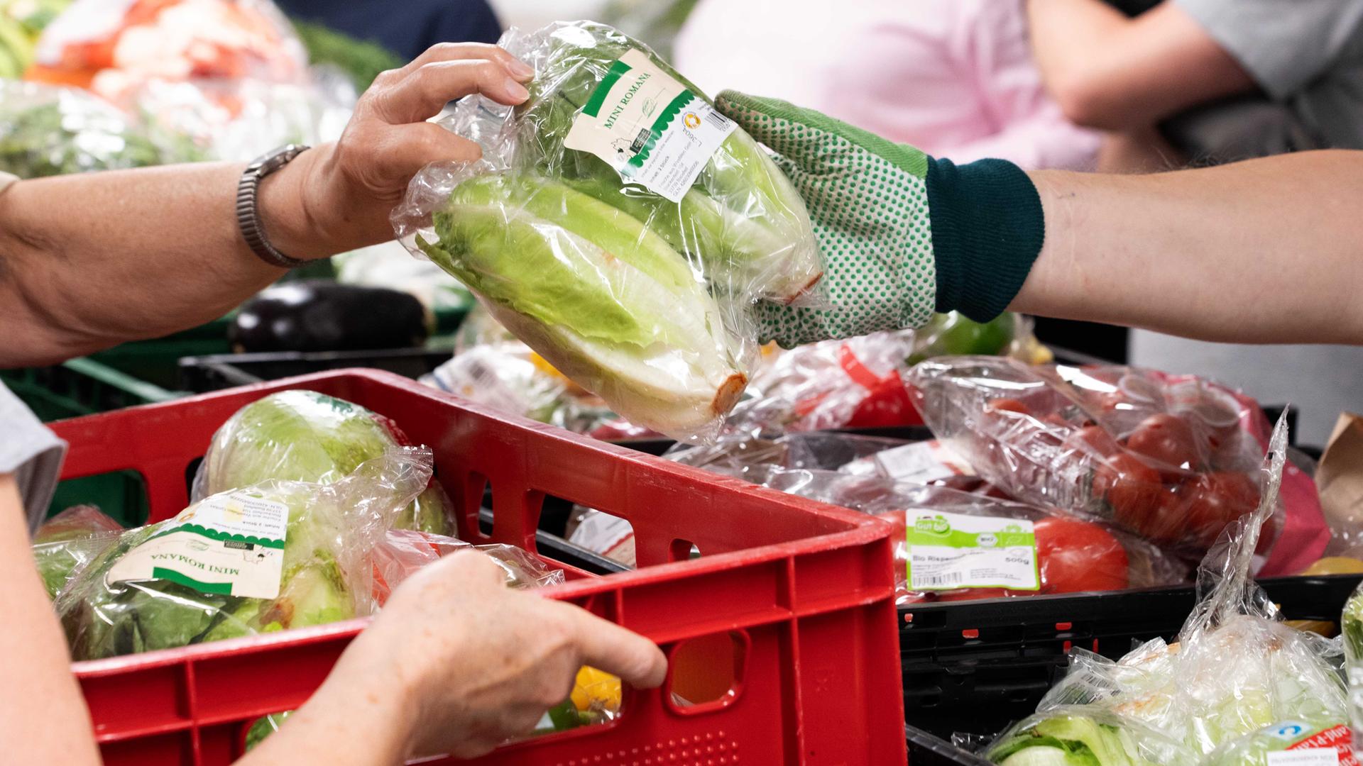 Mitarbeiter der Tafel bei der Lebensmittelausgabe, Obst und Gemüse wird von einer Hand in Handschuh weitergereicht.