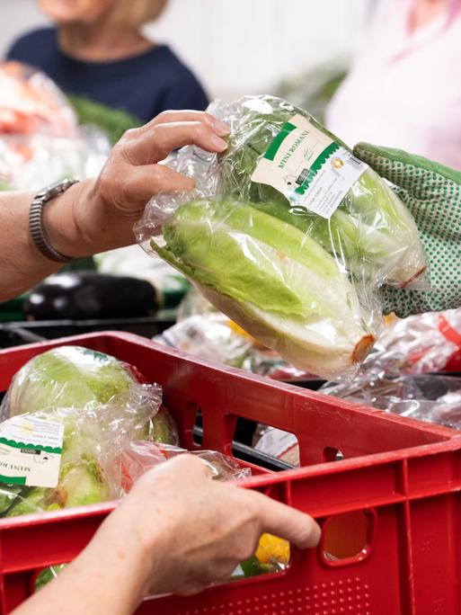 Mitarbeiter der Tafel bei der Lebensmittelausgabe, Obst und Gemüse wird von einer Hand in Handschuh weitergereicht.