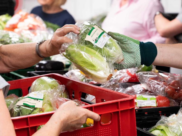 Mitarbeiter der Tafel bei der Lebensmittelausgabe, Obst und Gemüse wird von einer Hand in Handschuh weitergereicht.