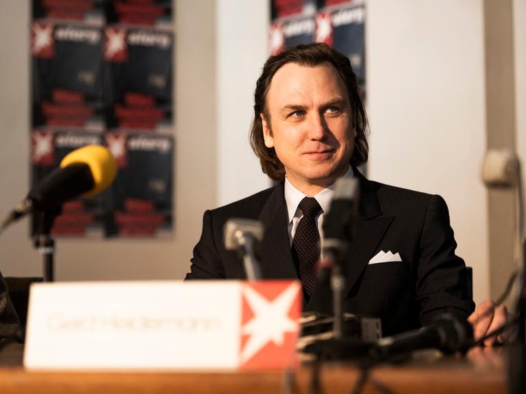 Schauspieler Lars Eidinger sitzt in seiner Figur des Reporters Gerd Heidemann in "Faking Hitler" bei einer Presskonferenz.