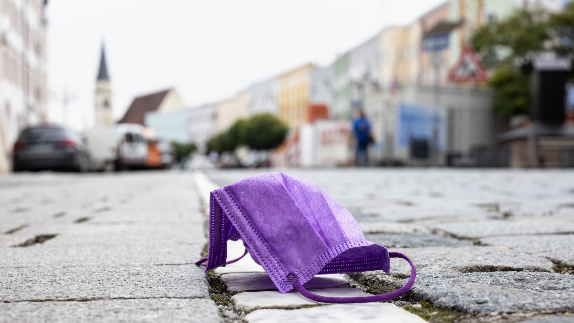 Eine violette medizinische Maske liegt auf einer Straße, während im Hintergrund die Altstadt von Mühldorf am Inn zu sehen ist. 