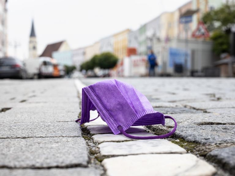 Eine violette medizinische Maske liegt auf einer Straße, während im Hintergrund die Altstadt von Mühldorf am Inn zu sehen ist. 