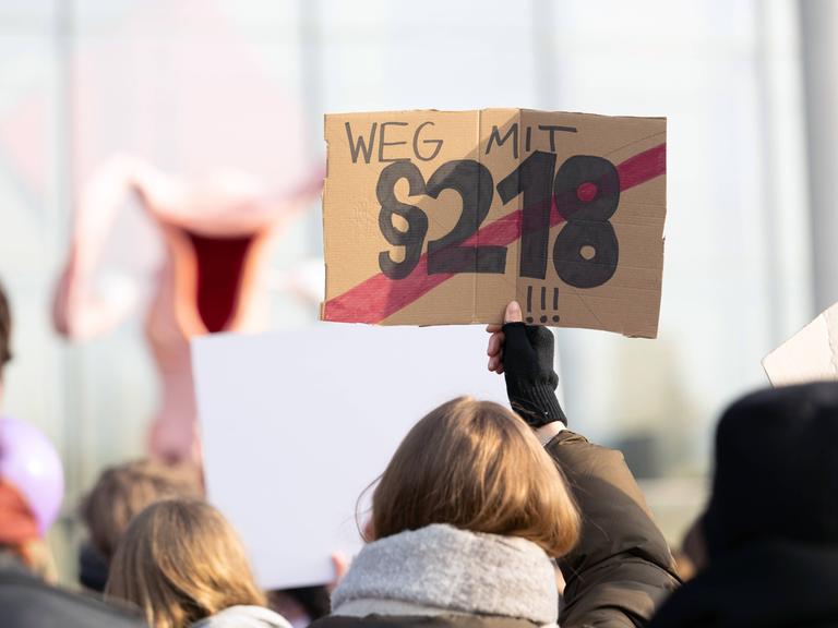 Frau hält Schild hoch, auf dem "§218" mit rot durchgestrichen ist