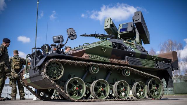 Ein Panzer mit Raketen. Bei dem Panzer stehen mehrere Männer. Sie tragen Militär-Anzüge. 