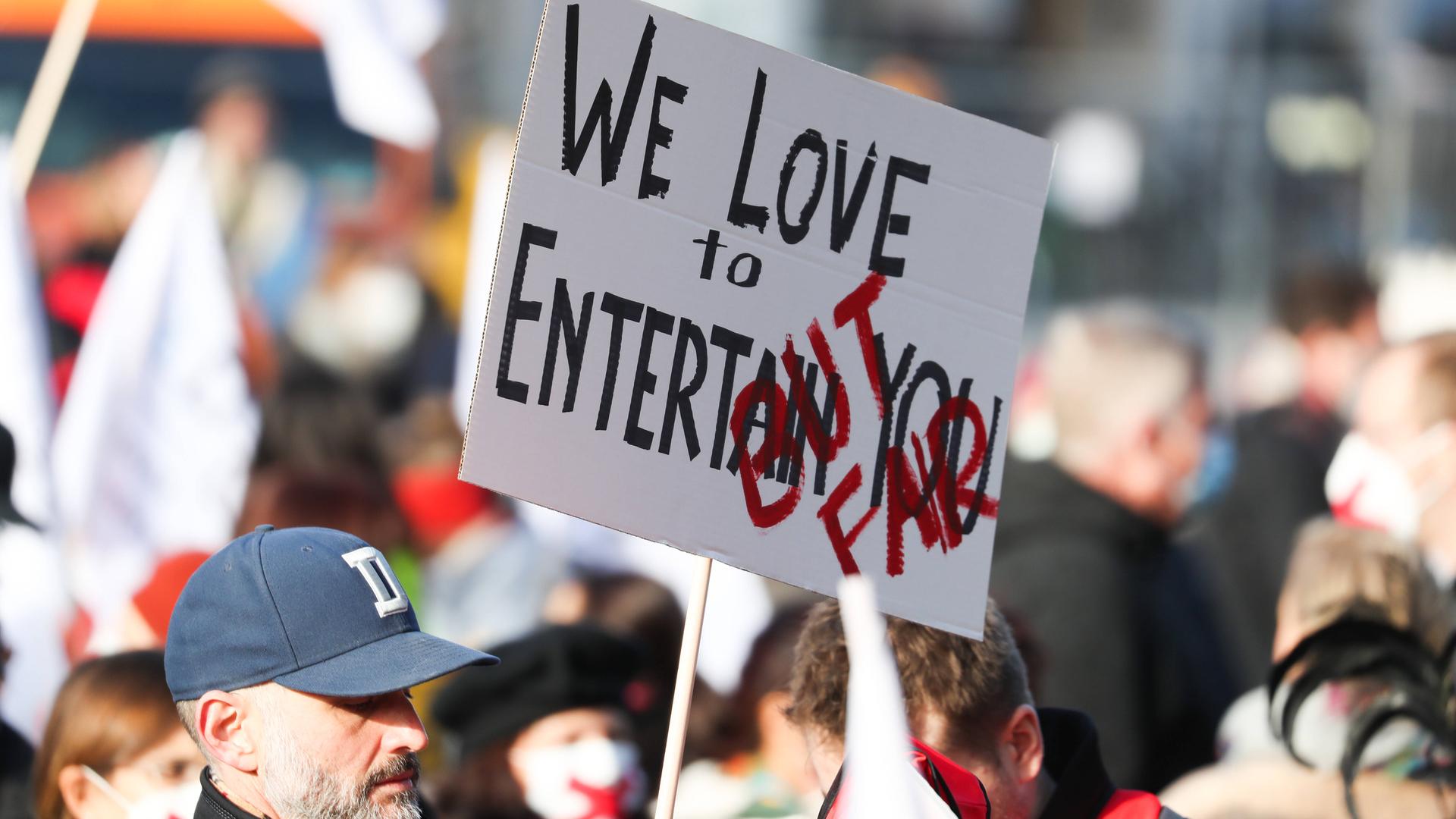 Hunderte Beschäftigte der Staatstheater aus Niedersachsen demonstrieren auf dem Opernplatz in Hannover gegen Kürzungen, ein Demostrant hät ein Schild: "We love to entertain you - but fair!", 10.11.2020. Hunderte Beschäftigte der Staatstheater aus Niedersachsen demonstrieren auf dem Opernplatz in Hannover gegen Kürzungen, ein Demostrant hät ein Schild: "We love to entertain you - but fair!", 10.11.2020.
