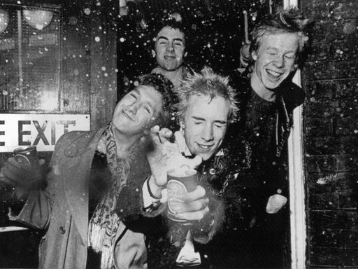 Das schwarz-weiß-Foto zeigt die britische Punk-Rock-Band „Sex Pistols“. Sie lassen am 3. Dezember 1976 in London eine Dose Bier explodieren. Vorne Steve Jones (l) und Bandleader und Sänger Jonny Rotten (M), dahinter Glen Matlock und Paul Cook (r).