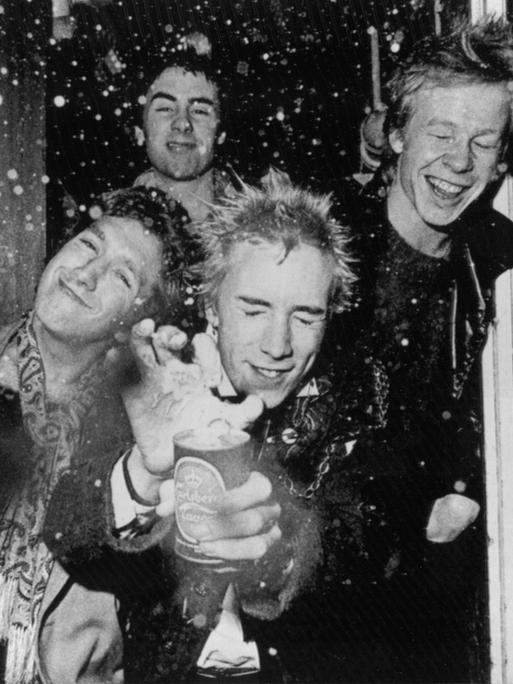 Das schwarz-weiß-Foto zeigt die britische Punk-Rock-Band „Sex Pistols“. Sie lassen am 3. Dezember 1976 in London eine Dose Bier explodieren. Vorne Steve Jones (l) und Bandleader und Sänger Jonny Rotten (M), dahinter Glen Matlock und Paul Cook (r).