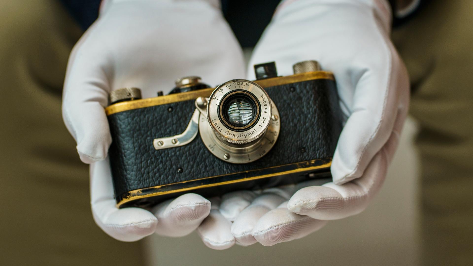 Zwei Hände in weißen Handschuhen halten ein Leica Kamera aus dem Jahr von 1924, Zwei Hände in weißen Handschuhen halten ein Leica Kamera aus dem Jahr von 1924,