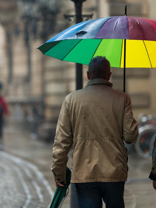Ein Paar mit einem bunten Regenschirm geht bei regnerischem Wetter eine Straße in der Dresdener Altstadt entlang. 