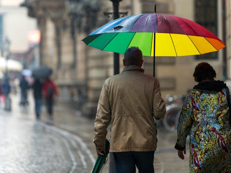 Ein Paar mit einem bunten Regenschirm geht bei regnerischem Wetter eine Straße in der Dresdener Altstadt entlang. 