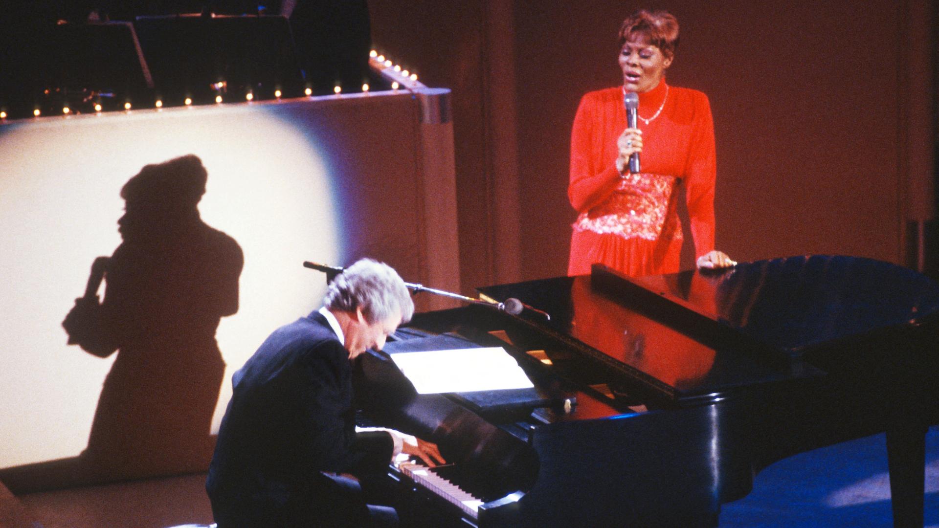 Der US-Komponis Burt Bacharach spielt am Klavier, neben ihm steht die Sängerin Dionne Warwick in einer Aufnahme vom Juni 1988