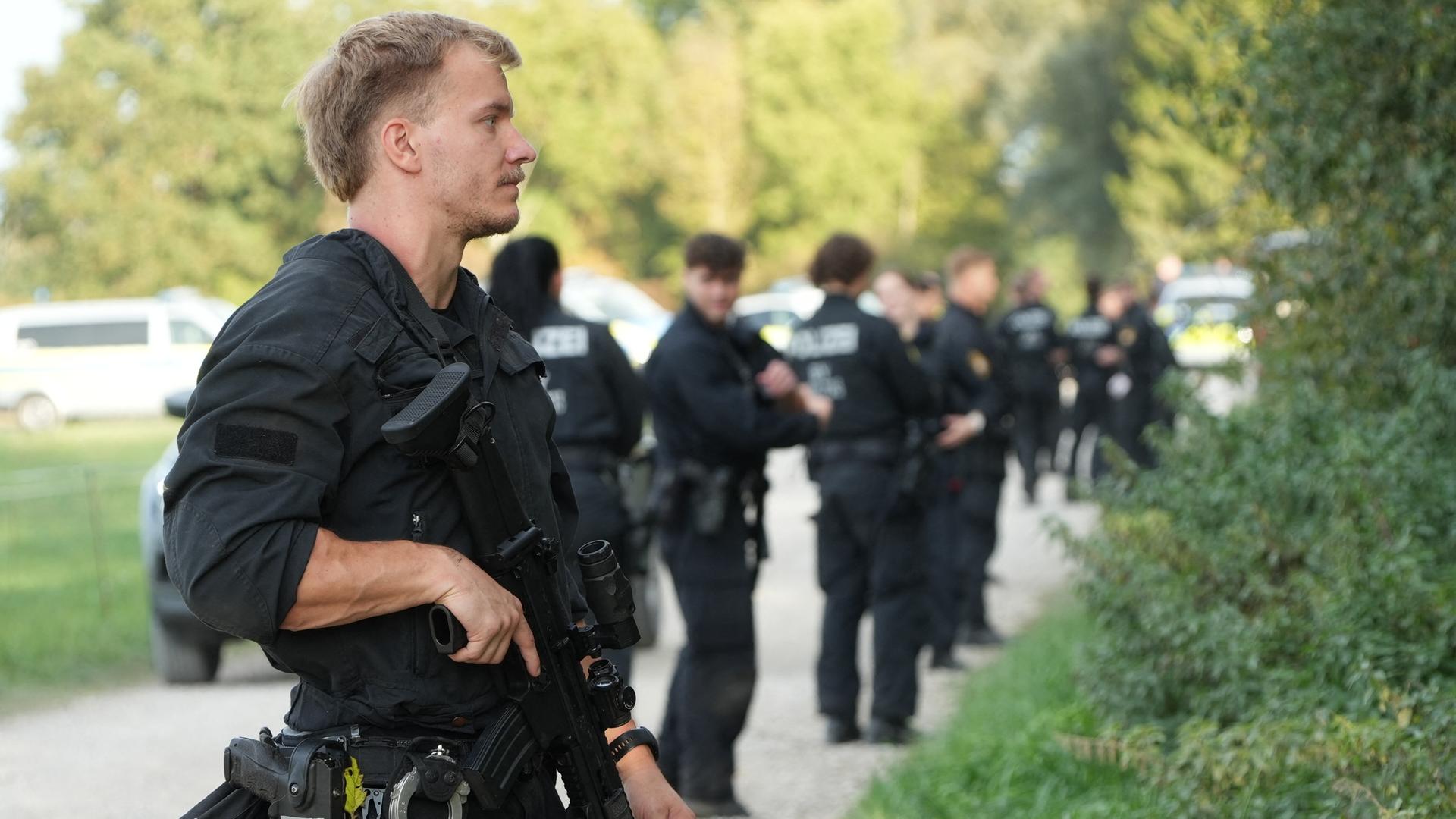 Mehrere Polizisten stehen am Rand eines Waldgebietes. Einer der Polizisten hat eine Waffe im Anschlag. Mehrere Polizisten stehen am Rand eines Waldgebietes. Einer der Polizisten hat eine Waffe im Anschlag.