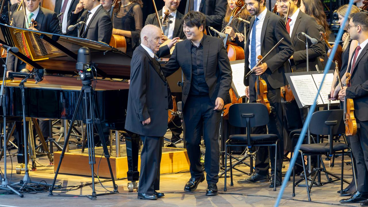 Daniel Barenboim und Lang Lang stehen vor Orchester-Musikern. Barenboim legt Lang Lang die Hand auf die Schulter.