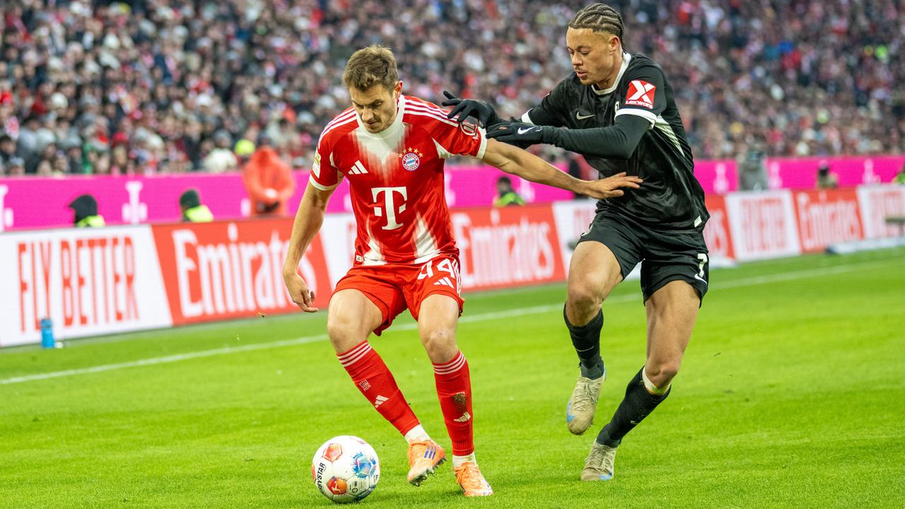 Josip Stanisic im roten Trikot vom FC Bayern München im Zweikampf mit Derry Scherhant vom SC Freiburg (schwarzes trikot) 22.11.2025