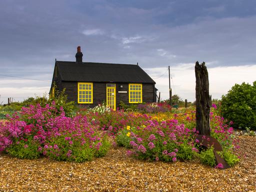 Das "Prospect Cottage" des britischen Malers und Filmemachers Derek Jarman in Dungeness. Ein Haus mit gelben Fensterrahmen inmitten eines blühenden Steingartens. 