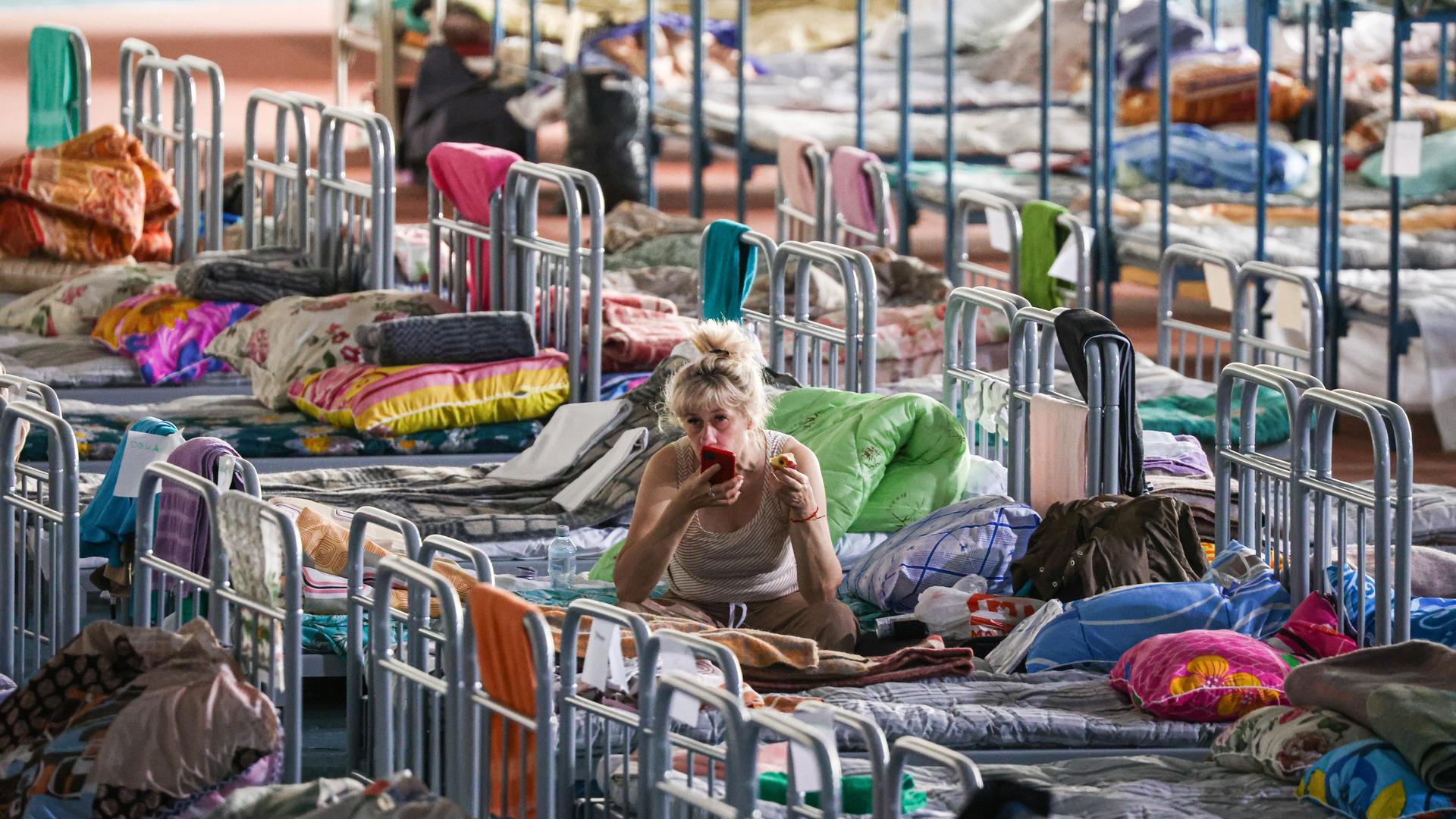Eine Frau sitzt auf einem von vielen Betten, die in Belgorod in einer Sporthalle aufgestellt wurden. Bild der russischen Staatsagentur Tass.