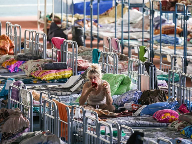 Eine Frau sitzt auf einem von vielen Betten, die in Belgorod in einer Sporthalle aufgestellt wurden. Bild der russischen Staatsagentur Tass.