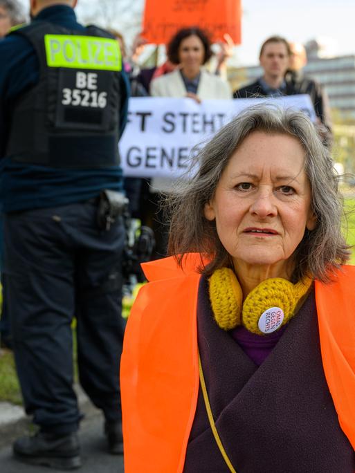 Marion Fabian (72, Künstlerin), im Hintergrund Polizei und sich solidarisierende Wissenschaftler bei der Blockade der Letzten Generation am Ernst-Reuter-Platz, Berlin, 28.04.23