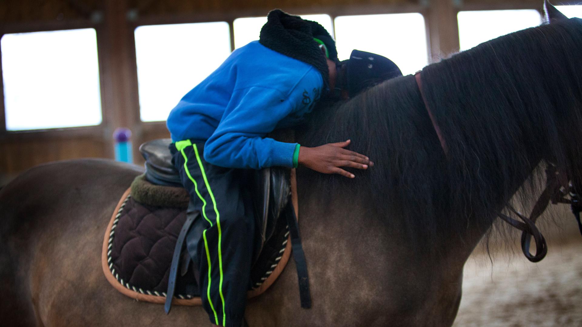 Ein Junge sitzt im Sattel und lehnt sich nach vorn, um sein Pferd zu umarmen.