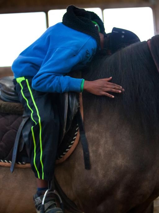 Ein Junge sitzt im Sattel und lehnt sich nach vorn, um sein Pferd zu umarmen.
