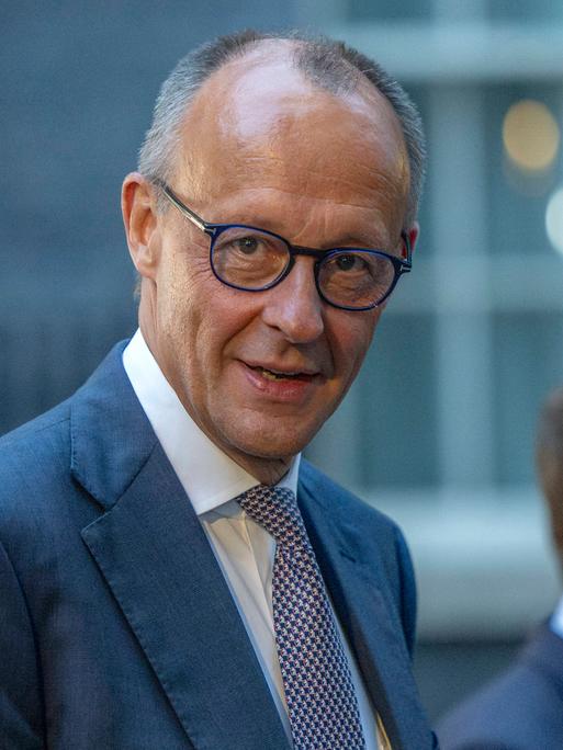 Kanzler Friedrich Merz schaut direkt in die Kamera, unscharf im Hintergrund Frankreichs Präsident Macron beim Ukraine-Gipfel in London am 7. Juni 2026