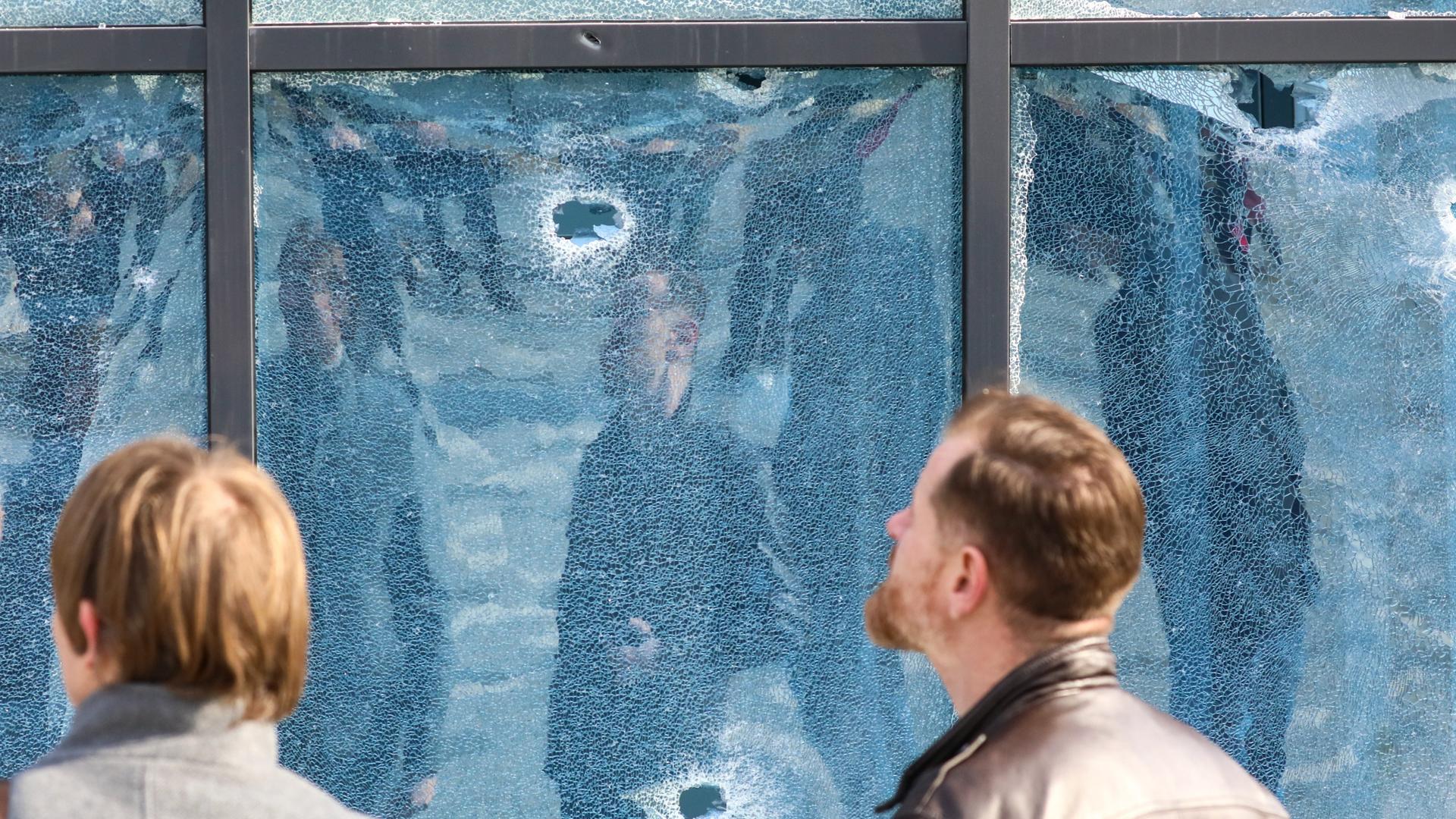 Zwei Menschen begutachten den durch eine landende Rakete verursachten Schaden in der Belgorod-Arena in Russland. In einer Glasfassade sind Einschusslöcher zu sehen. 