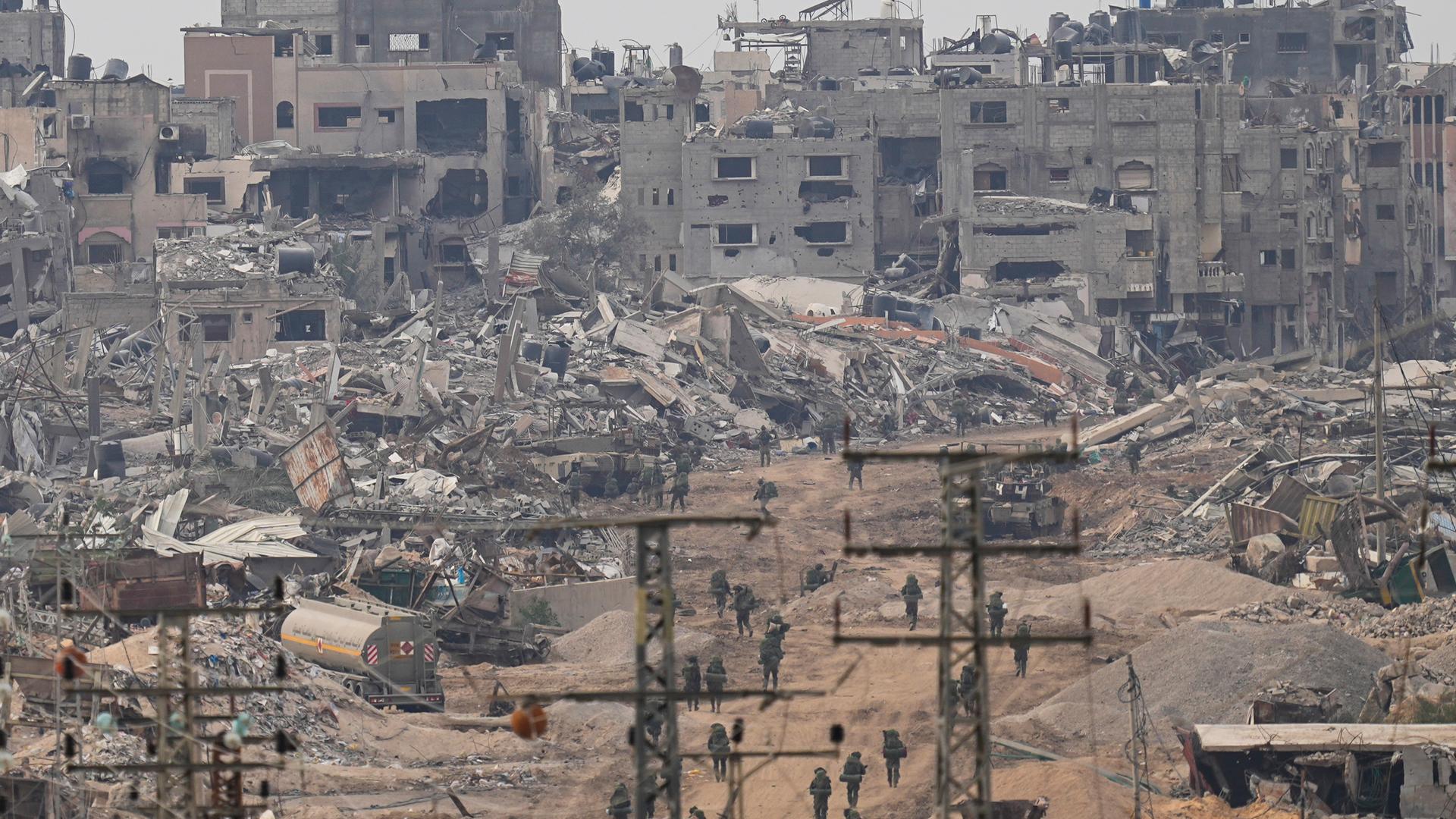 Israelische Soldaten laufen durch eine Straße im Gazastreifen. Im Hintergrund sind zerstörte Häuser zu sehen.