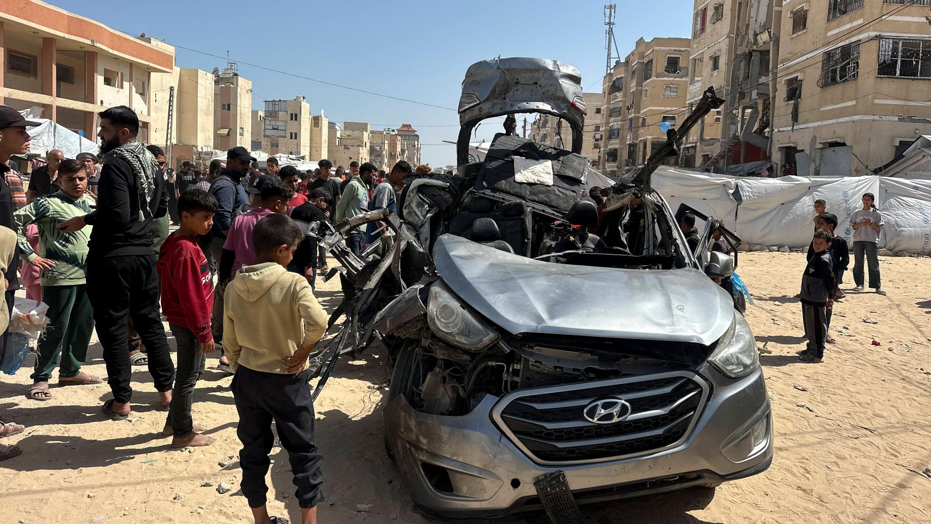 Mehrere Menschen stehen um ein schwer beschädigtes Auto in der palästinensischen Stadt Chan Junis im Gazastreifen.